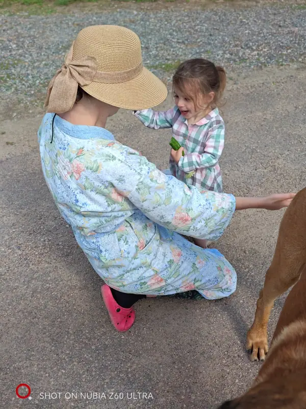 A mother in a sun hat crouching to talk with her small daughter, the family dog alongside